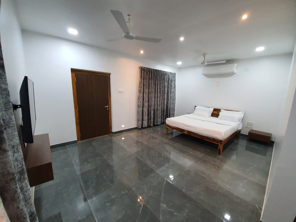 luxurious king suite with white bedsheet , blue curtains,fan and AC with lights on ceiling and grey flooring